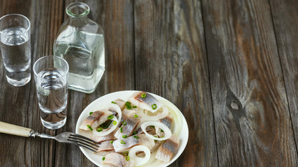 Vodka with salted herring and onion on wooden background. Alcohol pure craft drink and traditional snack. Negative space. Celebrating food and delicious.