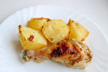 Appetizing baked chicken leg with potatoes on a white dish. Selective focus.