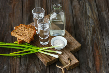 Vodka with green onion, bread toast and salt on wooden background. Alcohol pure craft drink and traditional snack. Negative space. Celebrating food and delicious.