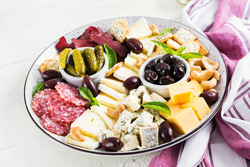Antipasto platter with basturma, salami, blue cheese, nuts, pickles and olives on a white wooden background.