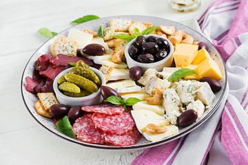 Antipasto platter with basturma, salami, blue cheese, nuts, pickles and olives on a white wooden background.