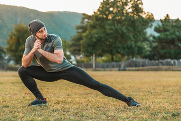 Sports and yoga. A man in sportswear performs stretching on the grass before training. Copy space