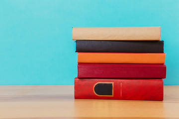 A simple composition of many hardback books, raw books on a wooden table and a bright blue background