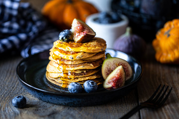 Pumpkin pancakes with syrup or honey, flax seeds, figs, blueberries in a dark plate on the table, selective focus