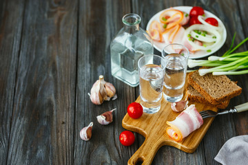 Vodka with lard and green onion on wooden background. Alcohol pure craft drink and traditional snacks, tomatos and bread toast. Negative space. Celebrating food and delicious.