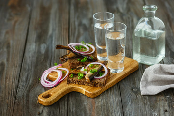 Vodka with fish and bread toast on wooden background. Alcohol pure craft drink and traditional snacks. Negative space. Celebrating food and delicious. Top view.