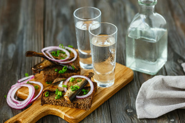 Vodka with fish and bread toast on wooden background. Alcohol pure craft drink and traditional snacks. Negative space. Celebrating food and delicious. Top view.