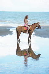 A pretty woman in a bikini is happily riding a horse on the beach.