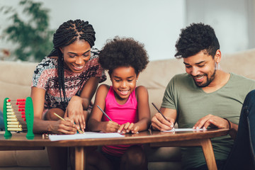 Mom and dad drawing with their daughter. African american family spending time together at home.