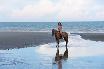 A pretty woman in a bikini is happily riding a horse on the beach.