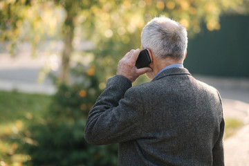 Back view of elderly man speak by the mobile phone outside