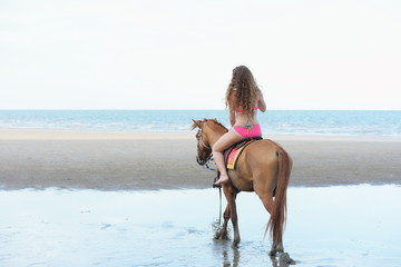 A pretty woman in a bikini is happily riding a horse on the beach.