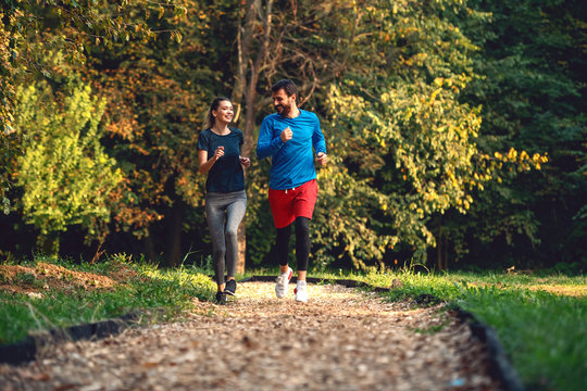 Full length of fit sporty happy caucasian couple in sportswear running in woods on trail in morning.