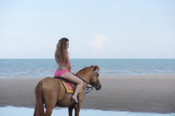 A pretty woman in a bikini is happily riding a horse on the beach.