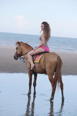 A pretty woman in a bikini is happily riding a horse on the beach.