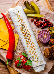 Shawarma with meat and vegetables lies on wooden table background