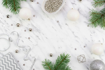 Flat lay frame Christmas festive arrangement made of silver decorative elements and xmas branches. Copy-space on a white marble background