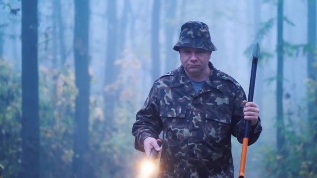 Brutal man with an ax and a flashlight walks through the forest