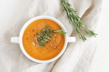 Pumpkin and carrot soup with cream,  seeds and rosemary herb on beige linen background. Copy space. Top view.
