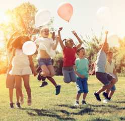 Happy children holding ballons and  jumping  together in park