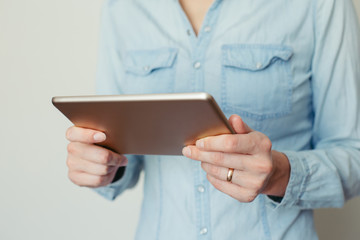 Image of a young woman working on a tablet computer at home on a background of light wall