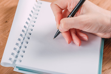 Close up of woman's hands writing in spiral notepad placed on wooden desktop with various items