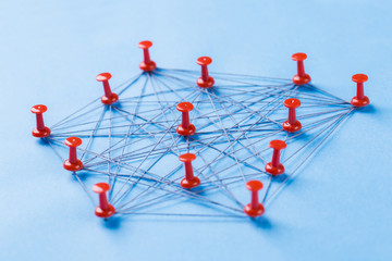 network with red pins and string, An arrangement of colorful pins linked together with string on a blue background suggesting a network of connections.