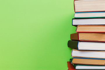 Simple composition of many hardback books, raw of books on wooden table and light green background