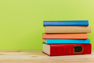 Simple composition of many hardback books, raw of books on wooden table and light green background