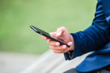 Closeup of male hands is holding cellphone outdoors on the street. Man using mobile smartphone.