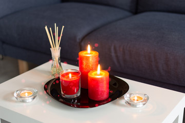 Room air refresher sticks and red burning candles on table on home modern interior.