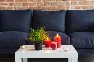 Room air refresher sticks and red burning candles on table on home modern interior.