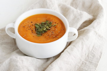 Pumpkin and carrot soup with cream and seeds on beige linen background. Copy space. Top view.