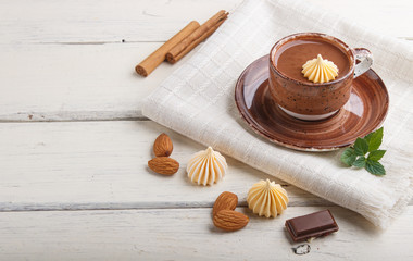 Cup of hot chocolate and pieces of milk chocolate with almonds on a white wooden background with linen napkin. side view