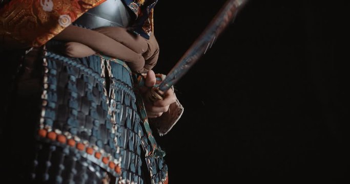 A man in japanese samurai armour is taking a sword out of his scabbaders, isolated on black background - martial arts, culture, traditions concept 4k footage