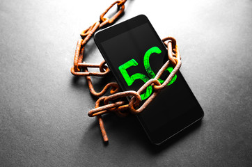 Rusty chains around the smartphone with 5g sign. Addicted to modern technologies.