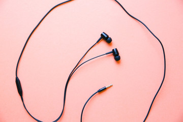 Earphones lying on the pink background. Modern music concept. Audio technology.