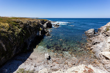 Fototapeta na wymiar Praia de pedras roladas protegida por penhascos da costa Alentejana em Portugal.