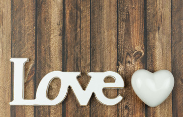 The word love in wooden letters with a white heart beside, wooden background