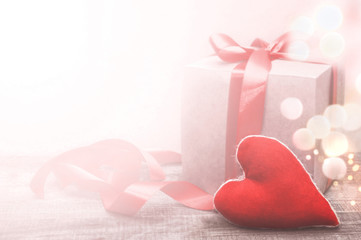 Red heart on a background of a gift box with ribbon and bow on a wooden board. Soft light with lights. Valentine's day concept congratulation