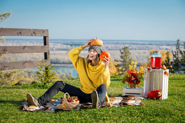 Young adult beautiful woman in nature on picnic with plaid, pumpkins and autumn scenery