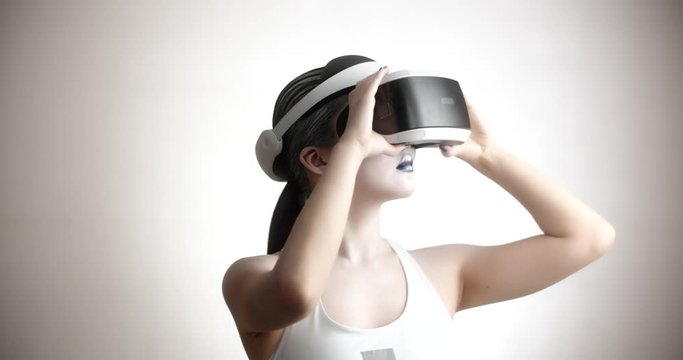 Young asian girl with bright artistic make-up wearing a vr helmet diving in world of vitual reality, moving her hands and interacting with it - technology concept closeup 4k footage