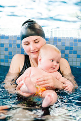 Young mother, swimming instructor and happy little girl in the pool. Teaches infant child to swim. Enjoy the first day of swimming in the water. Mom holds child preparing for diving. doing exercises