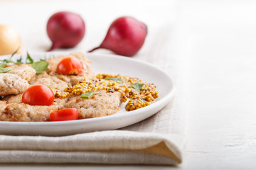Fried pork chops with tomatoes and herbs on a white ceramic plate on a white wooden background. side view, close up.