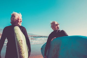 couple of seniors at the beach with black wetsuits holding a surftable ready to go surfing a the...