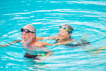 Fototapeta premium two seniors or mature caucasia people together at the swimming pool - active woman and man doing exercise together at the pool to be healthy - summer time in vacations