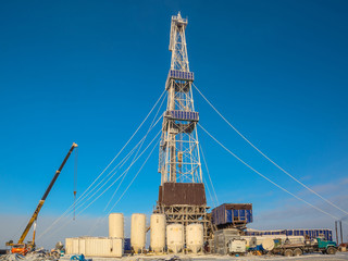 Drilling a well in winter at a northern oil and gas field. The drilling rig is covered in snow. The...
