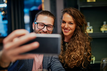 Cute caucasian fashionable couple sitting in restaurant at dinner and taking selfie.