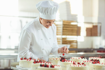 Confectioner is holding a cake in her hand in the bakery.