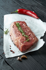 Raw fresh meat on paper with herbs, pepper and garlic on dark background